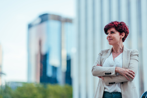 A confident female business person with short red hair is standing in the street posing for the camera