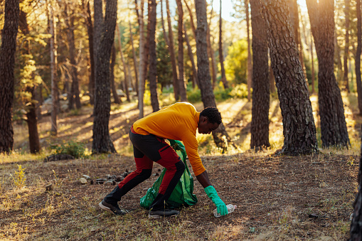 A young African American man is cleaning the woods of plastic trash that campers have left behind.