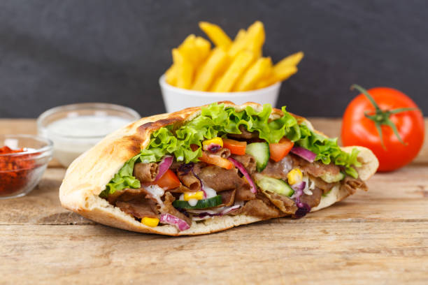Döner Kebab Doner Kebap fast food meal in flatbread with fries on a wooden board stock photo