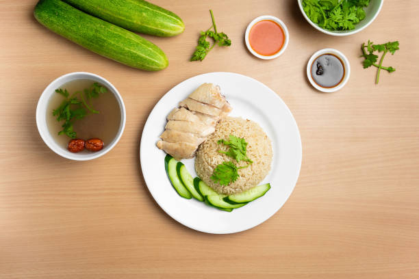 Steamed Chicken Rice with raw cucumber, Coriander, salad, sauce and soup served in a dish isolated on wooden background top view stock photo
