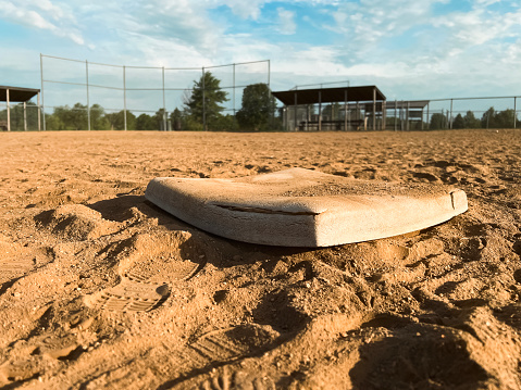 Low-angle view of second base covered with dirt and well-worn. Background of an empty baseball field with cleat shoe imprints.