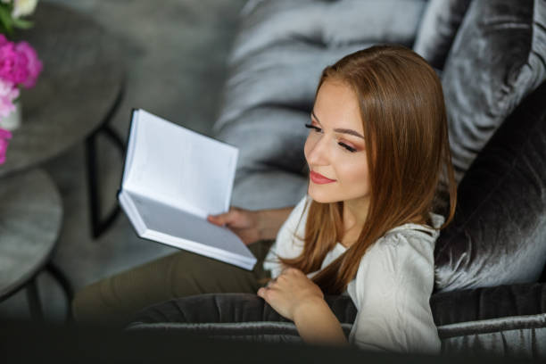 istock Redhead woman holding book and thinking at home 1406247241