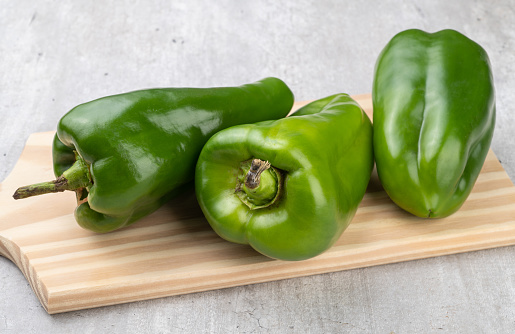 Three green bell peppers over wooden board.
