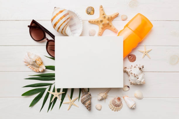 istock Summer time concept with blank greeting card and blank white paper on colored background. Seashells from ocean shore in the shape of frame separated with space for text top view 1406250228