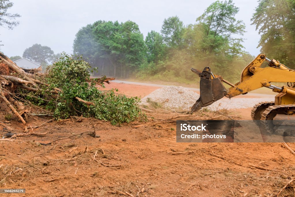 During the uprooting of trees and deforestation, a tractor is working the process to prepare the land for new house construction. During the uprooting of trees and deforestation, a tractor is working the process to prepare the land for new house construction in subdivision complex Glade Stock Photo