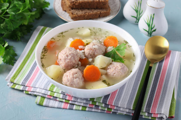 Soup with chicken meatballs, rice and vegetables in a white bowl on a blue background, Close-up stock photo
