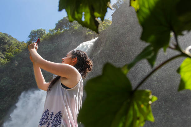 istock Smiling young woman with her closed eyes taking a selfie beside waterfall 1406258126
