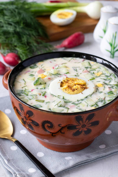 Traditional cold soup okroshka with sausage, radish, green onion and kefir served with boiled egg on brown bowl stock photo