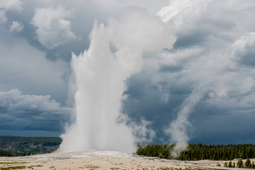 Old Faithful Geyser in the Upper Geyser Basin in Yellowstone National Park, Wyoming. An eruption with water and steam in the sky.