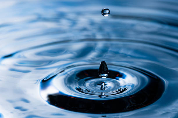 226.Droplet falls into water forming splash and concentric ripples. Deep blue reflections highlight fluid motion, surface tension, and wave propagation.
