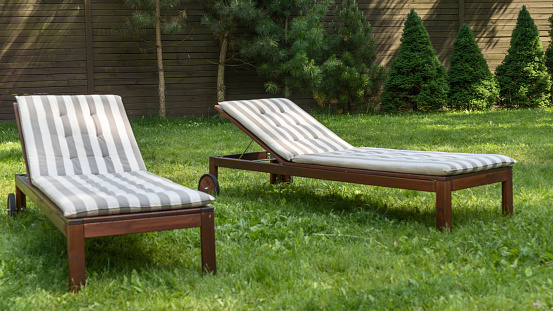 Lounge chairs on the backyard in a beautiful garden. Two empty sunbeds on the grass. Concepts of recreation, tanning in yard.