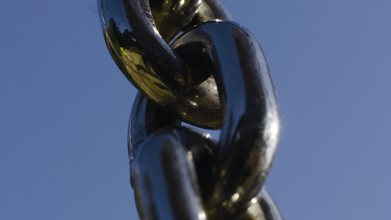 Reflection in black chain on background blue sky. Action. Close-up of black chain with reflection of greenery and sun glare on background blue sky.