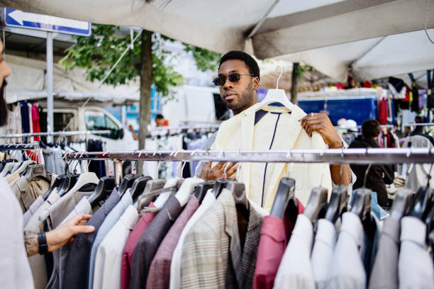 deux hommes qui achètent des vêtements dans un rack d’un marché aux puces - dépôt vente photos et images de collection