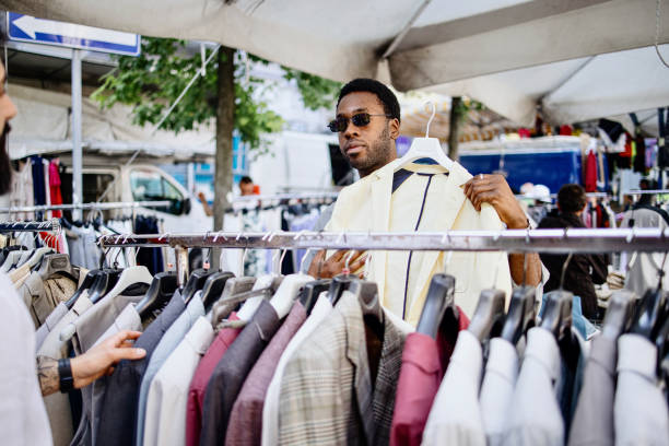 Two men shopping clothes from a rack at a flea market Male friends shopping in a second hand market in summer, zero waste concept second hand stock pictures, royalty-free photos & images