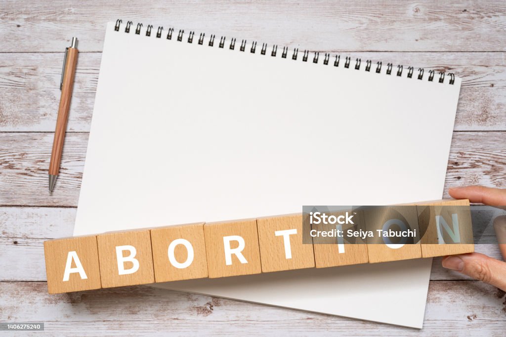 Wooden blocks with "ABORTION" text of concept, a pen, and a notebook. Abortion Stock Photo