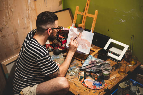 istock Guy with glasses painting an orange eagle with a brush on a small canvas in the studio 1406275909