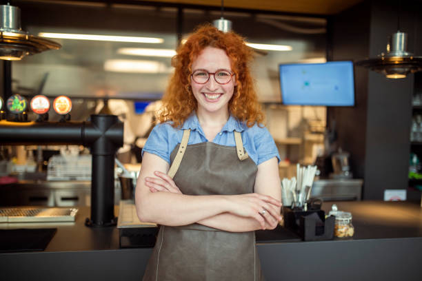 A view from the waist up of a redhead waitress standing next to the restaurant's cash register. stock photo