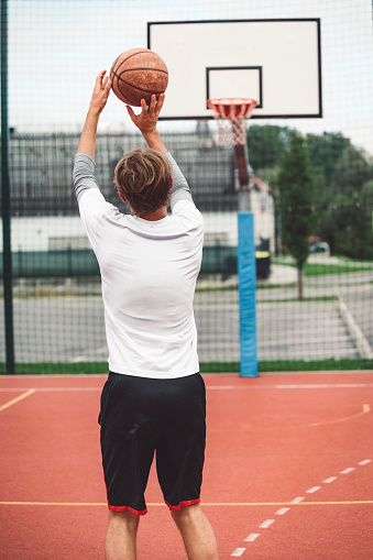 Young caucasian man with blonde hair shooting for the hoop. Young man holding a basketball, ready to shoot.