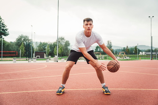 Young athlete dribbling a basketball on outdoors basketball court. Young man practicing his game.