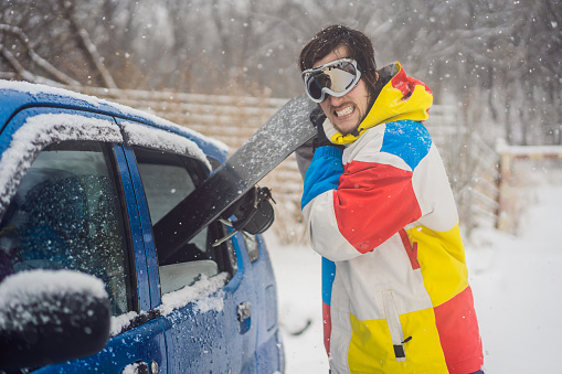 The snowboard does not fit into the car. A snowboarder is trying to stick a snowboard into a car. Humor, fun.