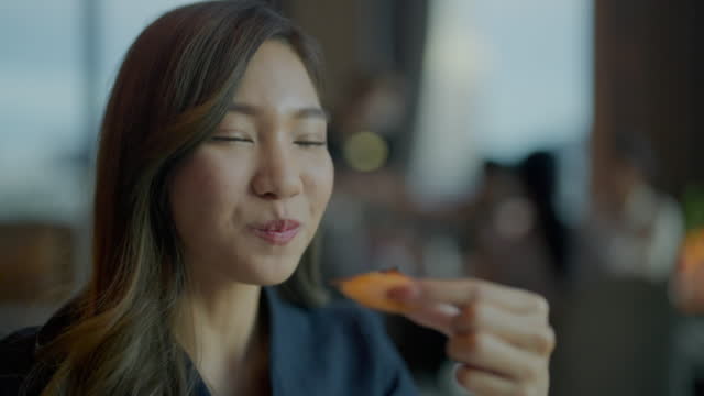 Headshot portrait of young Asian woman enjoying tasty food in restaurant.