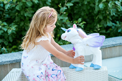 Adorable little girl playing with unicorn. Preschool child having fun with soft stuffed toy.