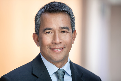 Portrait of mature multiracial Asian businessman in office hallway smiling