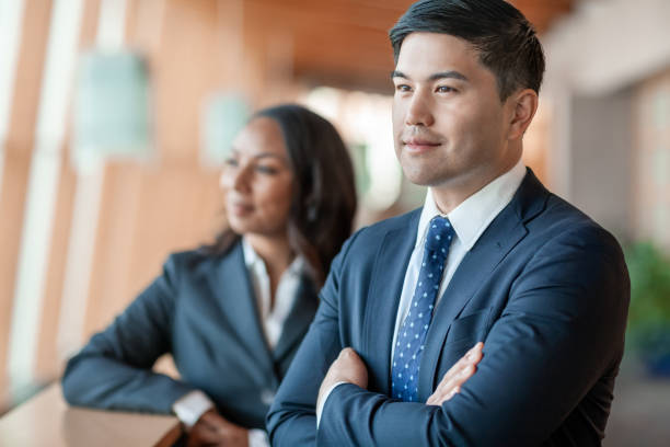Portrait of Pacific Islander ethnicity mid adult businessman with multiracial Black female coworker standing on balcony looking away stock photo