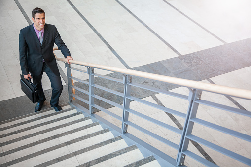 Hispanic mid adult businessman with briefcase about to climb a stairway at new office job