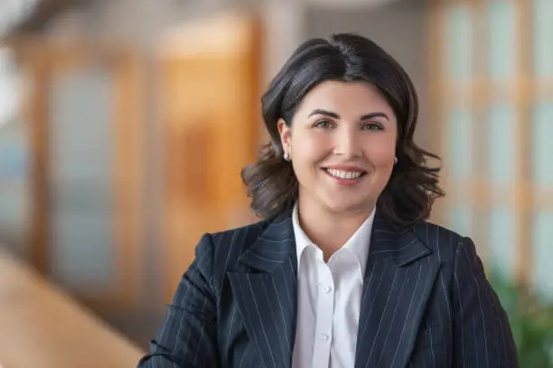 Photo of Portrait of young Caucasian businesswoman smiling at camera in office lobby in business suit