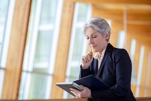 Portrait of serious senior Caucasian businesswoman leaning on railing in office balcony with day planner