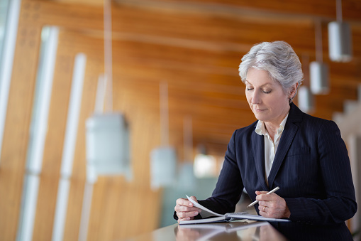 Portrait of senior Caucasian businesswoman leaning on railing in office balcony with day planner