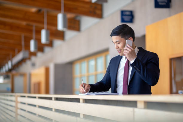 Portrait of Pacific Islander ethnicity businessman talking on cellphone taking notes on note pad stock photo