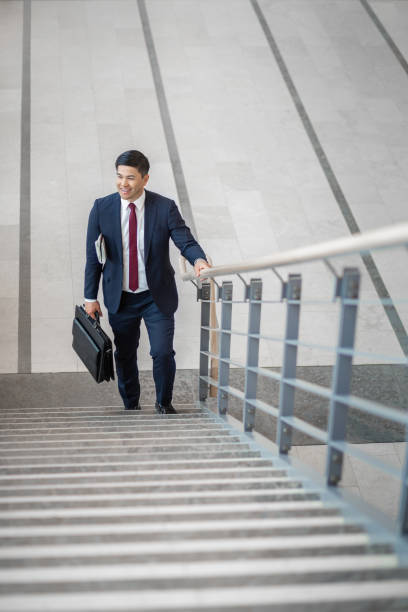istock Pacific Islander ethnicity businessman with briefcase climbing a staircase in office lobby 1406310304