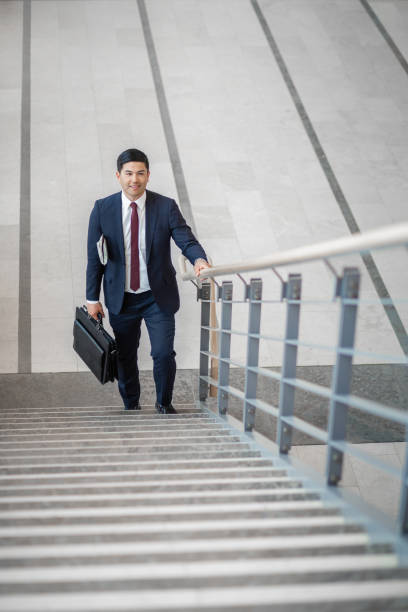 istock Pacific Islander ethnicity businessman with briefcase climbing a staircase in office lobby 1406310316