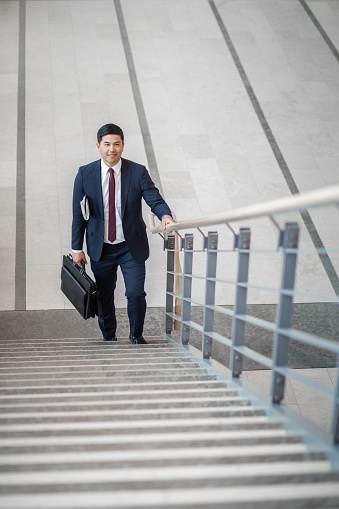 Pacific Islander ethnicity businessman with briefcase climbing a staircase in office lobby