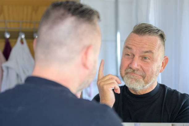 istock Senior man looking at his reflection with a rueful smile 1406313424