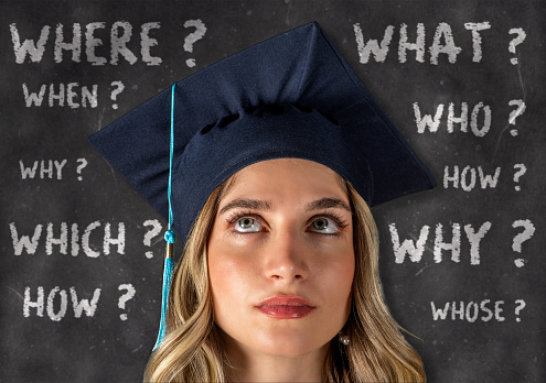 Young graduate woman wearing a cap in front of chalkboard has questions