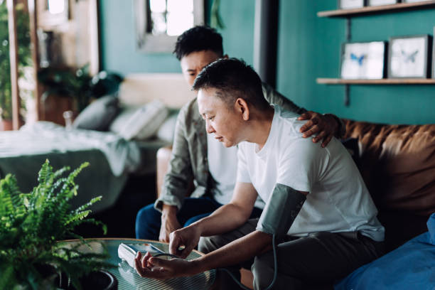 Senior Asian man checking blood pressure with his son at home. Looking worried. Son caring for his retired father, putting hand on his shoulder, comforting and consoling his father. Family love, care, elderly and healthcare concept hombre asiático mayor que se revisa la presión arterial con su hijo en casa. parece preocupado. hijo cuidando a su padre jubilado, poniendo la mano sobre su hombro, consolando y consolando a su padre. concepto de amor familiar, cuidado, ancianos y atenci