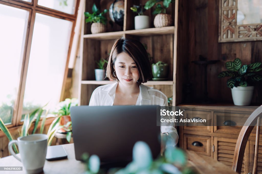 Young Asian female freelancer working online on laptop computer from home office. Businesswoman, entrepreneur, blogger, freelancer working from home concepts in cozy atmosphere. Lifestyle and technology Electronic Banking Stock Photo