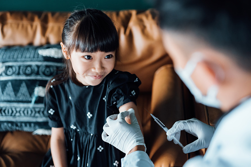 Young Asian girl getting vaccinated in medical clinic. Child vaccination and healthcare concept