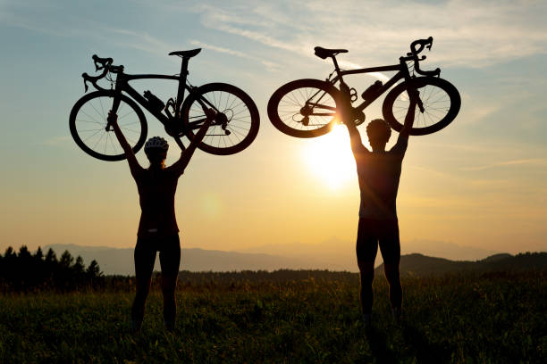 istock Two silhouettes holding bicycles high above heads, in winner pose 1406319739