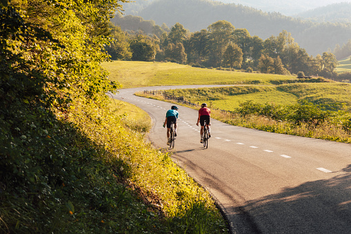 Two road cyclists, male and female during training at beautiful nature landscape at sunset, back view