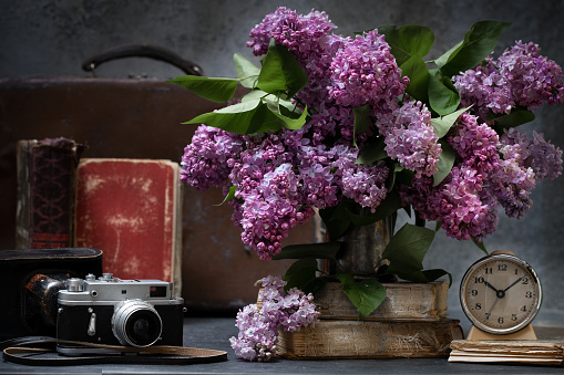 Bunch of lilac flowers with a vintage suitcase, old books and vintage alarm clock.