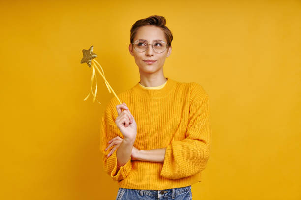 Playful woman holding magic wand and looking thoughtful stock photo