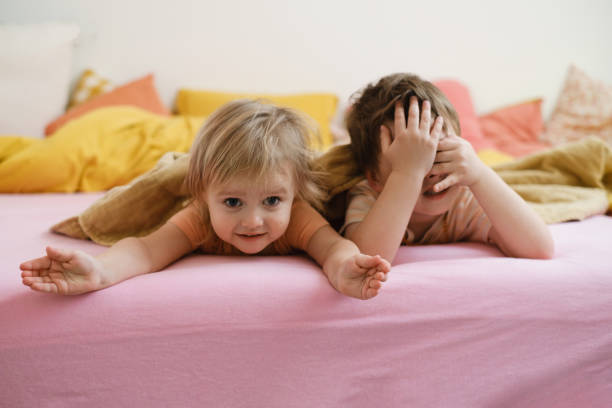 Happy kids playing on colorful bed in the morning kids playing on colorful bed in the morning hide-and-seek. Happy child Lie on pink bed. Sister and brother in bedroom, copy space. toddler siblings smiling, closed eyes matrass stock pictures, royalty-free photos & images