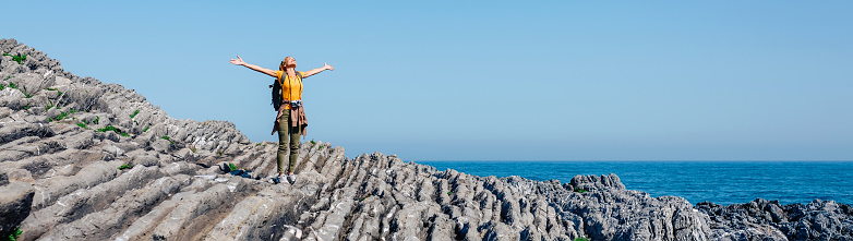 Young woman raising arms hiking through flysch rock landscape. Freedom concept