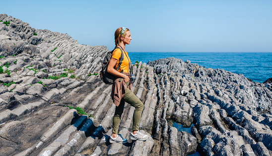 Young woman with backpack walking through flysch rock landscape