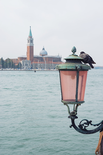 Traditional venetian lamppost and view of San Giorgio Maggiore island. San Giorgio Maggiore is one of the islands of Venice, lying east of the Giudecca and south of the main island group. Its Palladian church is an important landmark. It has been much painted, featuring for example in a series by Monet.