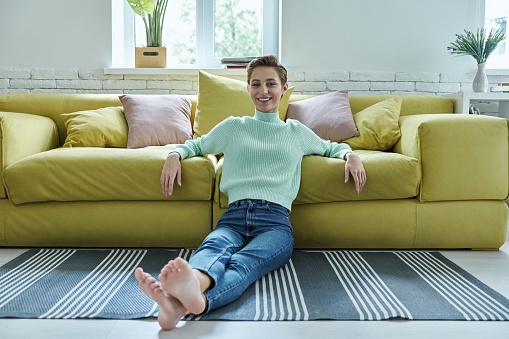 Carefree young woman smiling while sitting on the floor at home